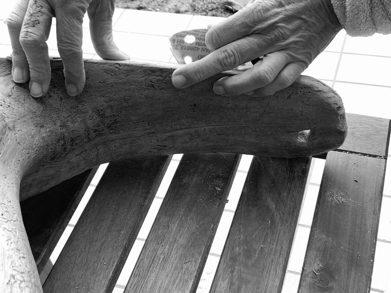 Mani che reggono ed esaminano un pezzo di legno curvo su una panca a doghe.