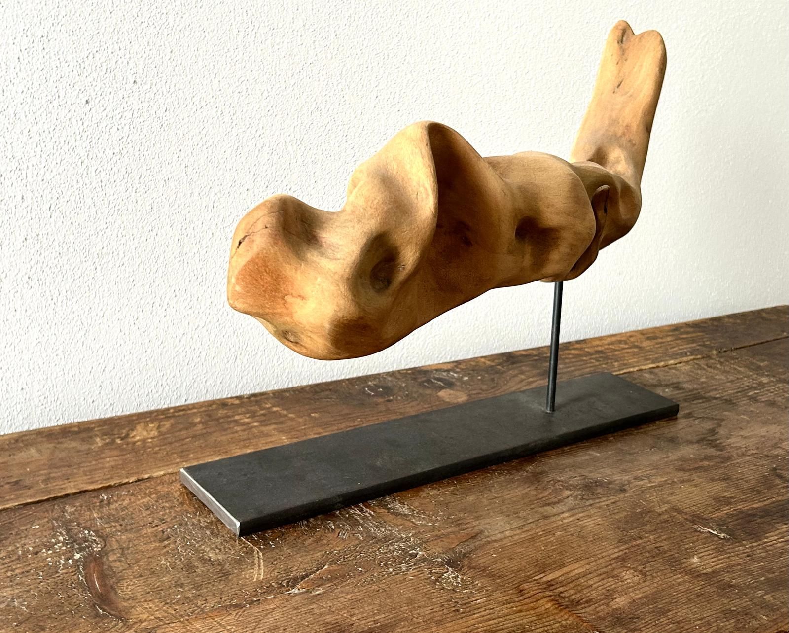 Scultura astratta in legno su un supporto nero, contro una parete bianca.
