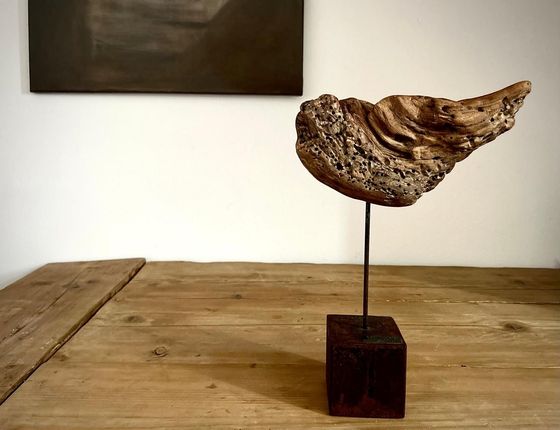 Scultura astratta su un tavolo di legno, con una forma ruvida simile a una roccia su una sottile asta di metallo e una base scura.