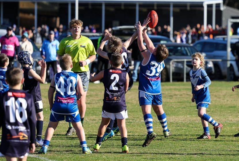 A group of young boys are playing a game of aussie rules football on a field.