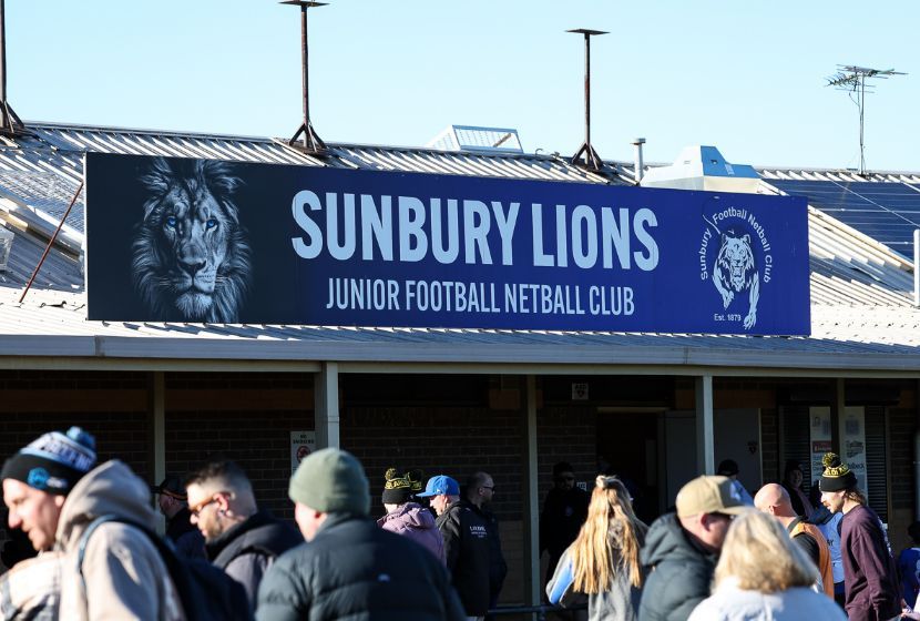 A group of people are standing in front of a sign that says sunbury lions junior football netball club.