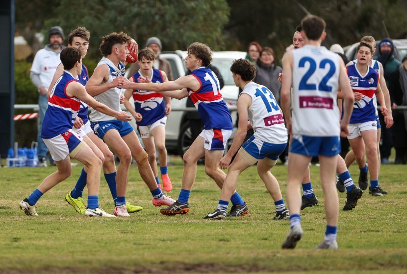 A group of young men are playing a game of aussie rules football on a field.