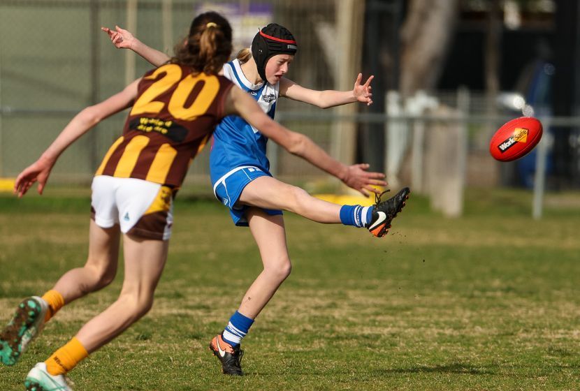 A girl wearing a number 20 jersey kicking a afl football ball