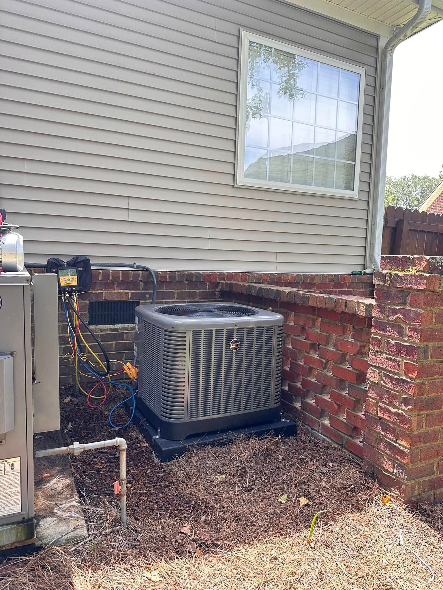 Outdoor air conditioner unit beside a brick wall and house siding, with gravel ground and a window above