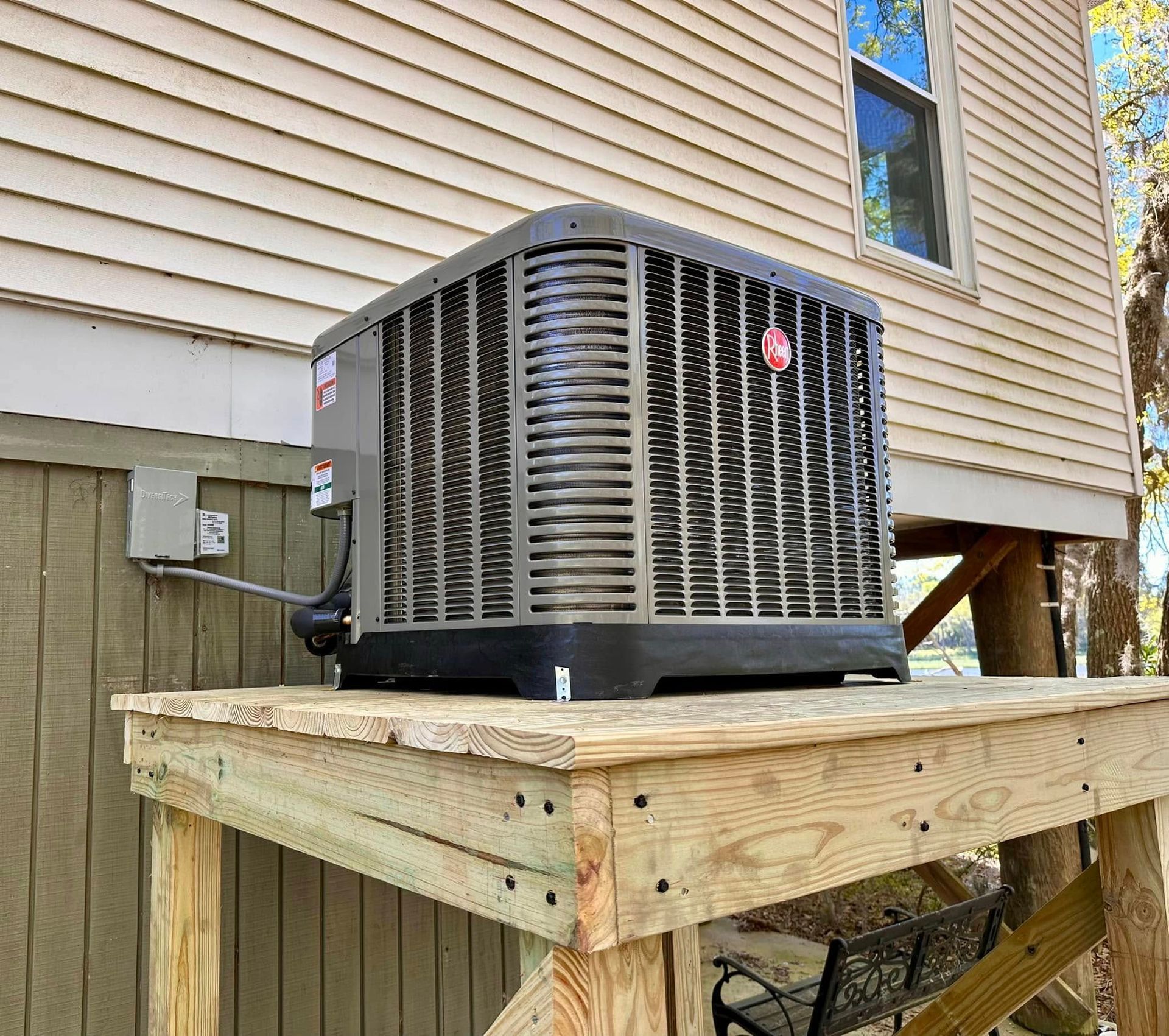 Outdoor HVAC unit on a wooden platform beside a beige house wall