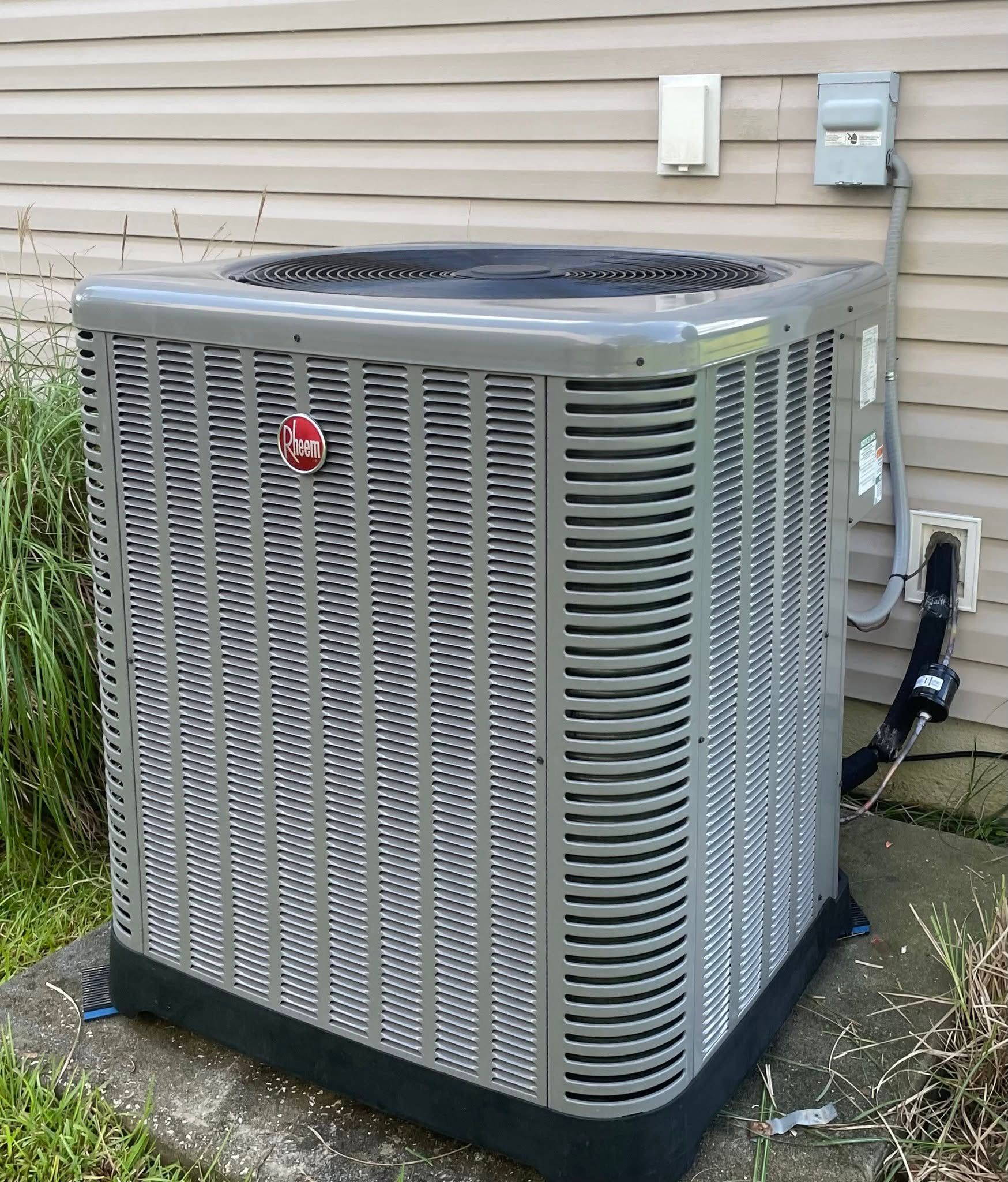 Outdoor air conditioner unit beside a house with beige siding and utility boxes on the wall