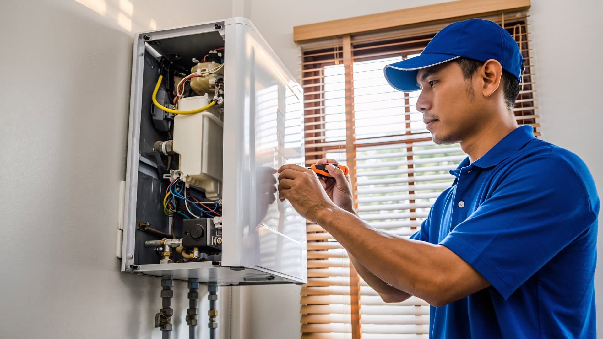 Technician in blue uniform inspecting an open electrical panel indoors.