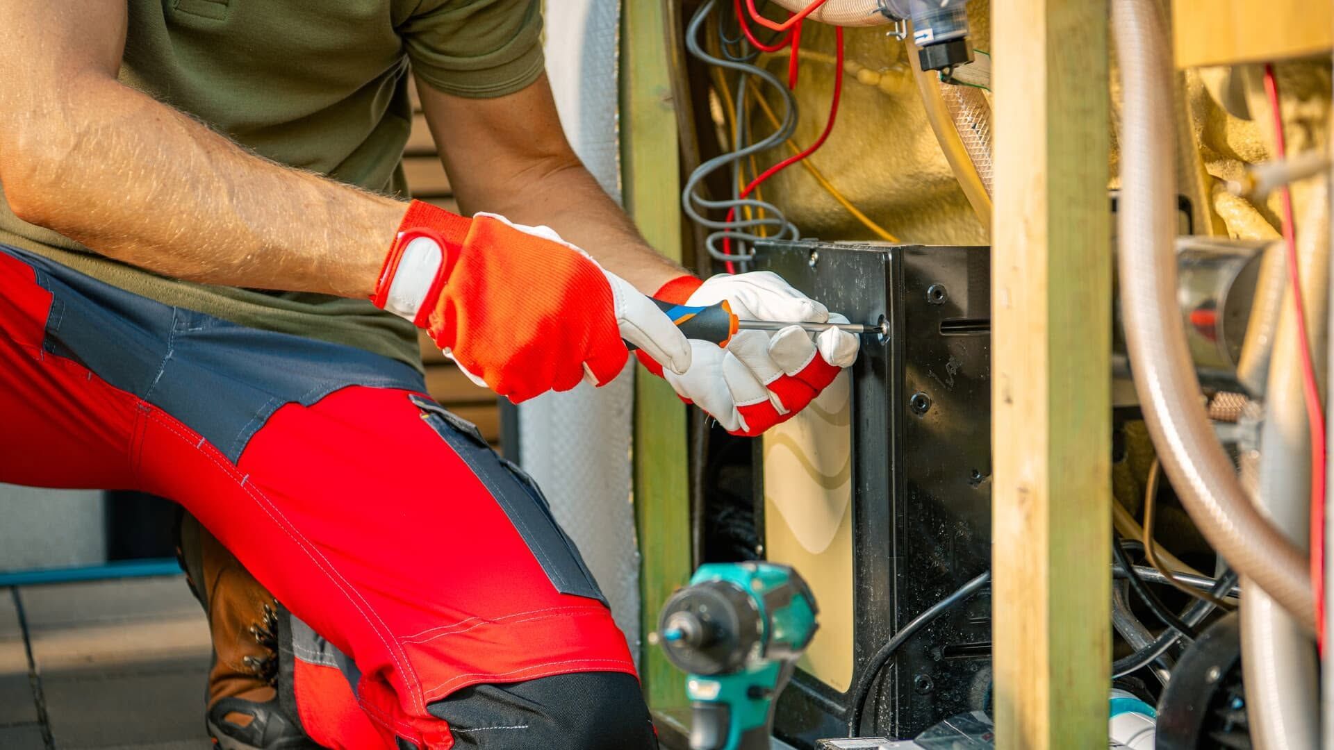 Worker in red gloves using a tool to repair wiring inside machinery cabinet