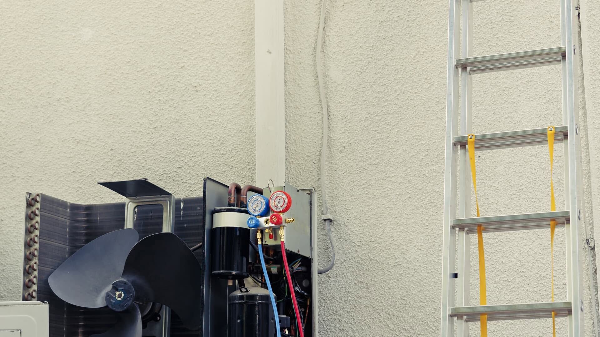 Outdoor equipment beside a wall, with a fan unit and a yellow ladder leaning nearby.