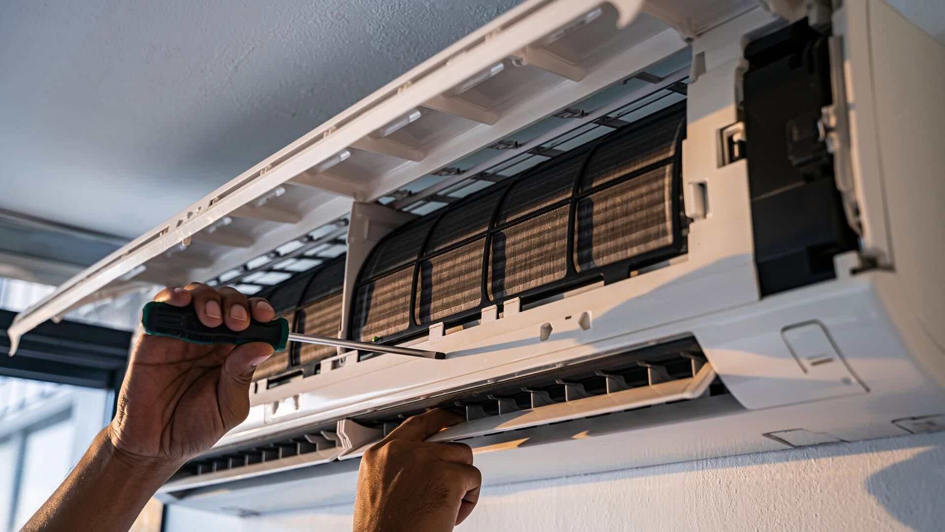 Technician cleaning the open filter of a wall-mounted air conditioner with a brush
