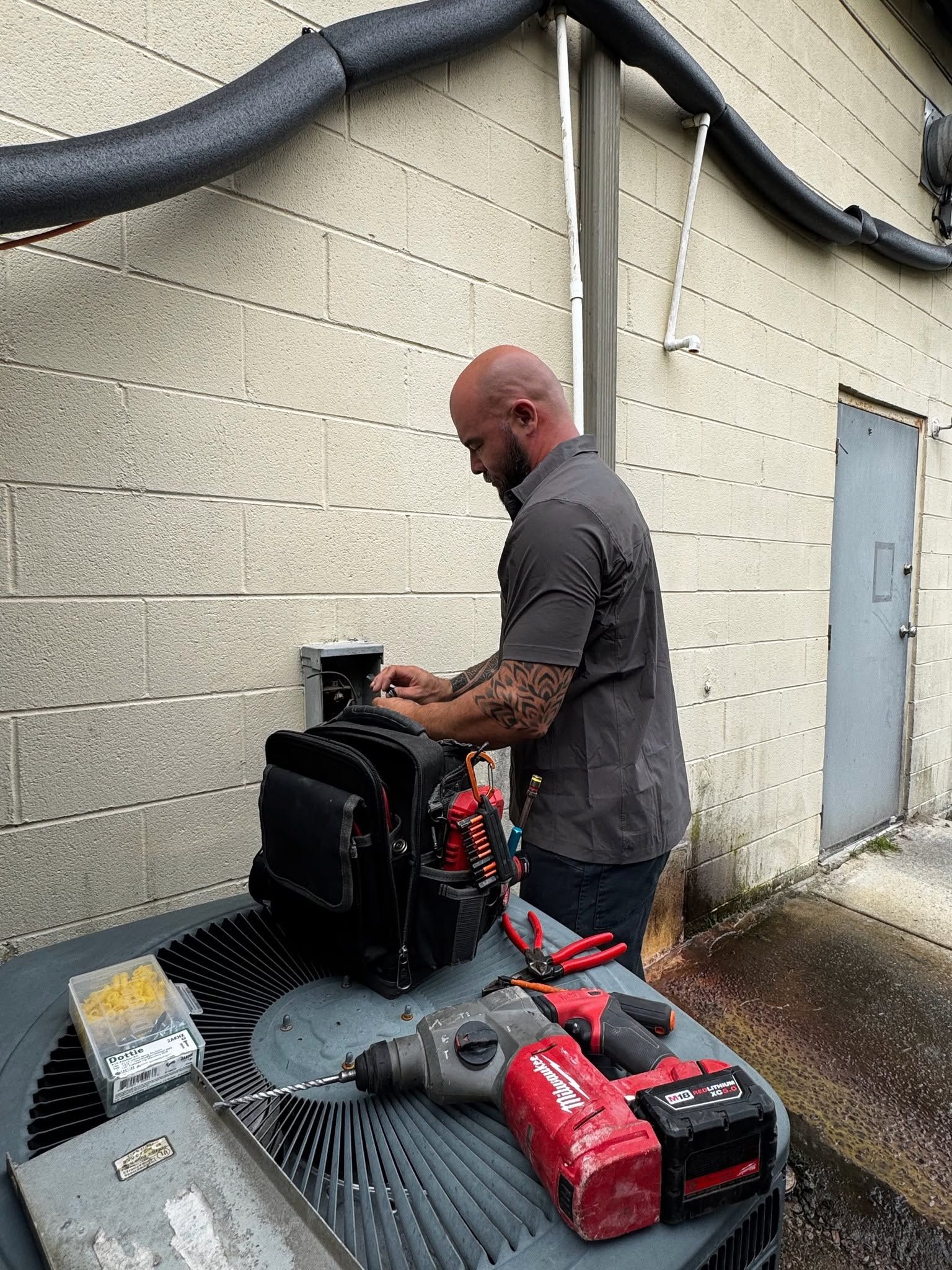 Technician working beside outdoor wall with black tool bag and red power tools on a gray table