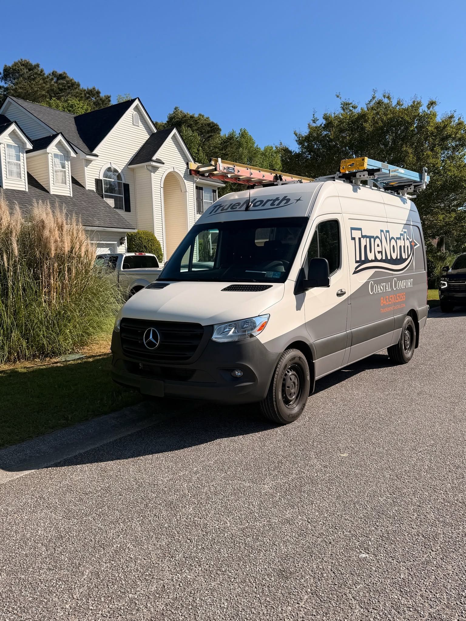 White delivery van parked on a driveway beside houses on a sunny residential street.