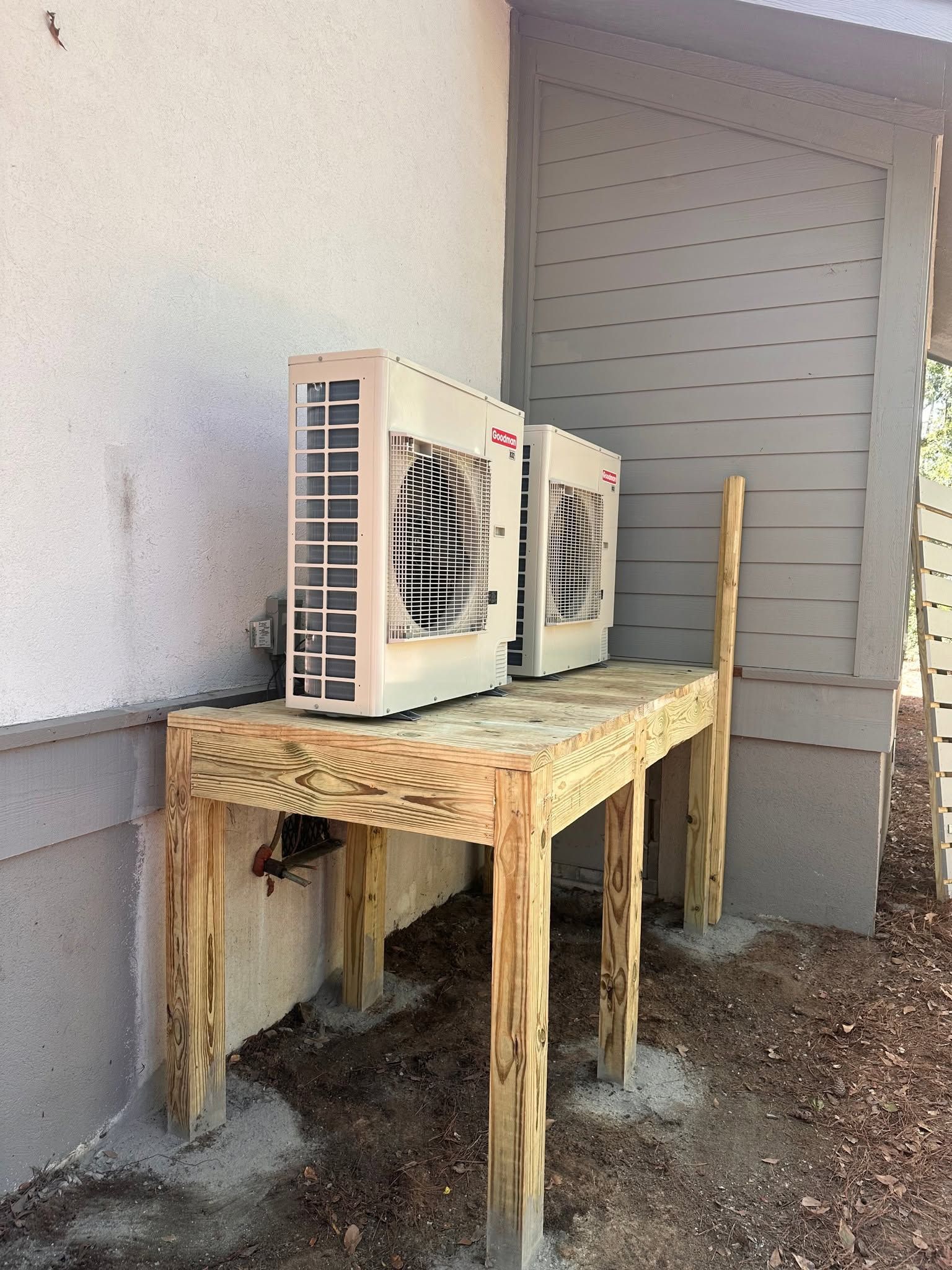 Outdoor air conditioner unit on a weathered wooden table beside a building wall and door