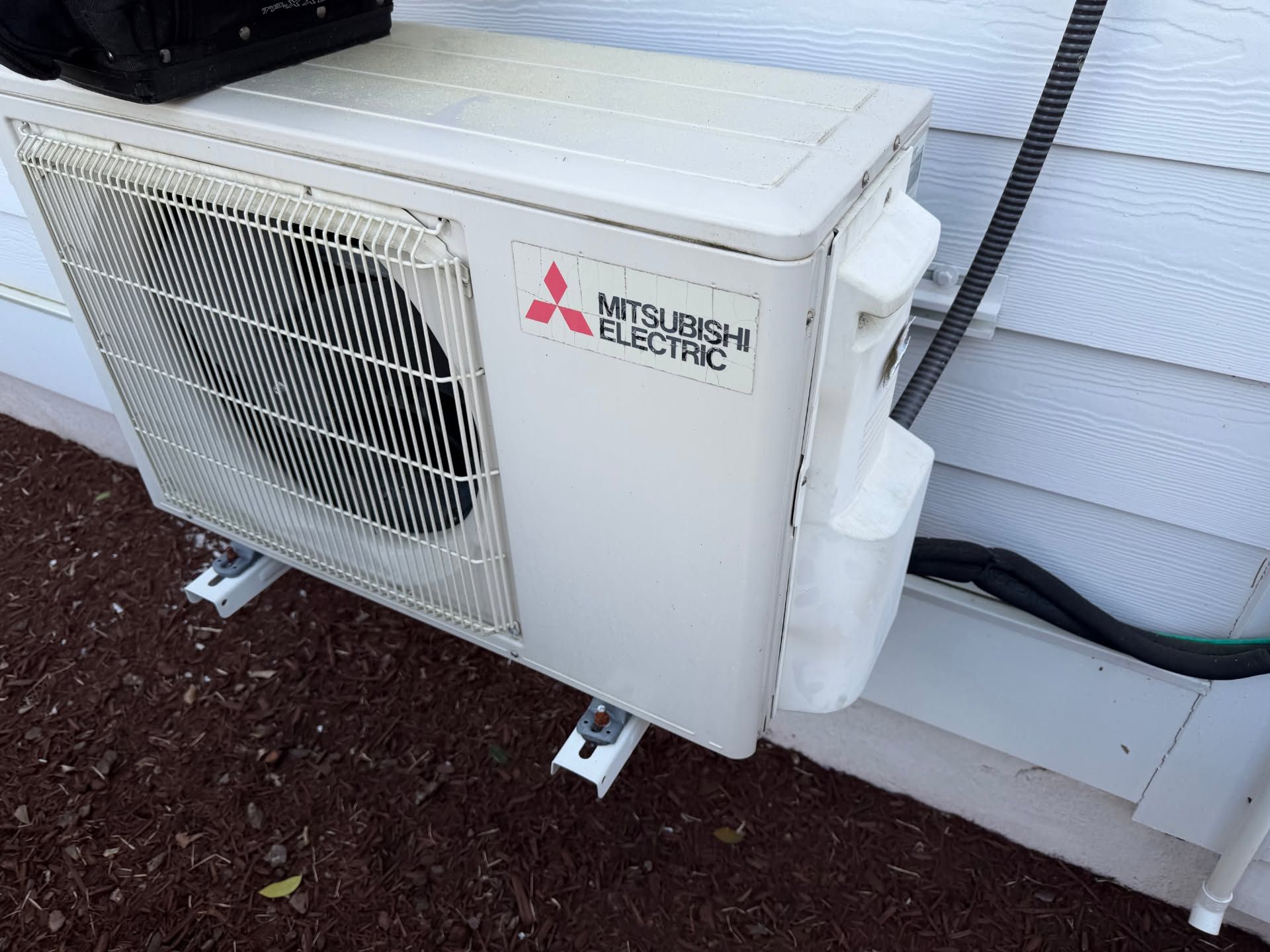 Outdoor Mitsubishi Electric AC unit beside a house wall on red gravel with exposed tubing