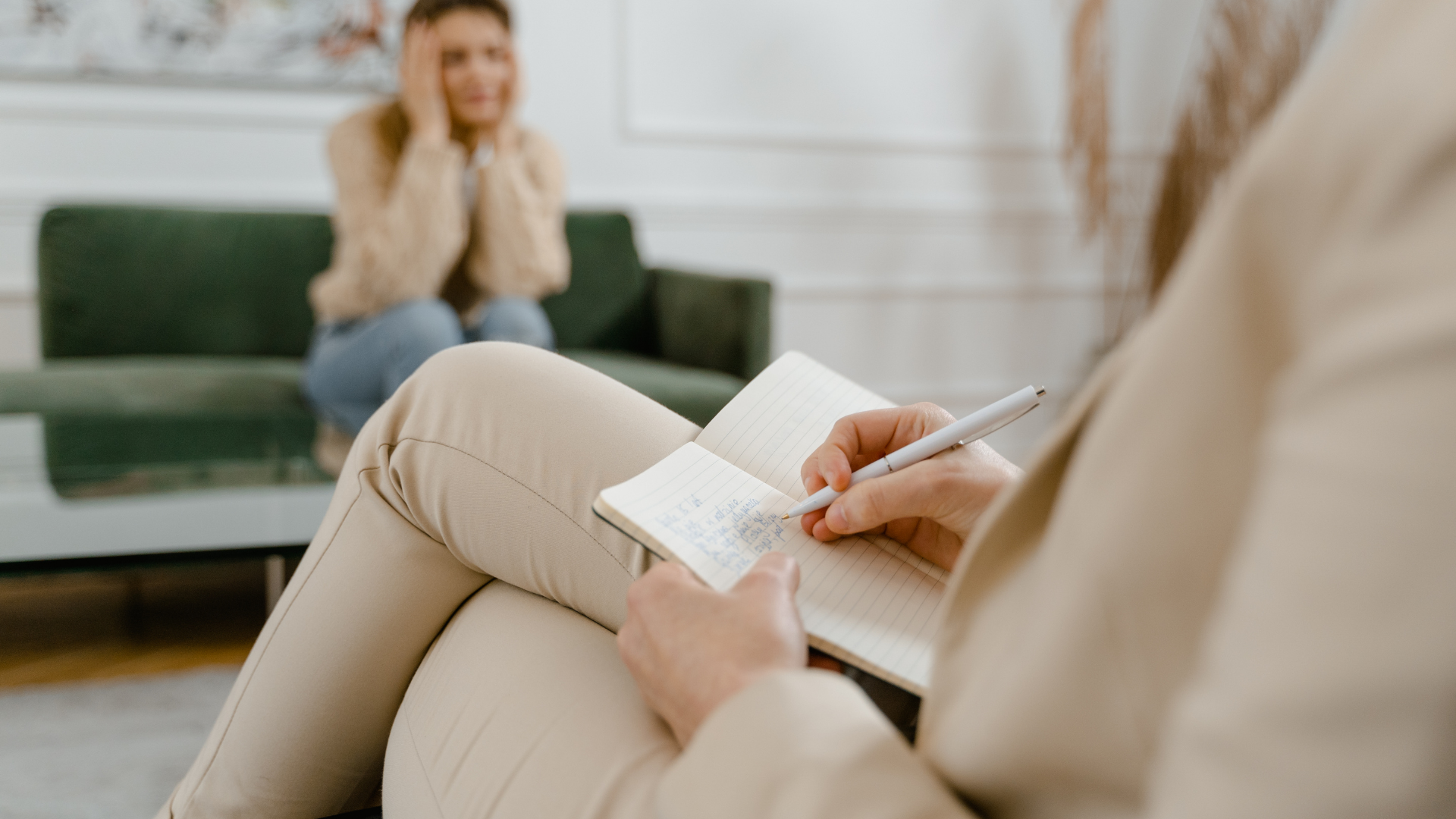 Therapist taking notes while a distressed client sits on a couch.