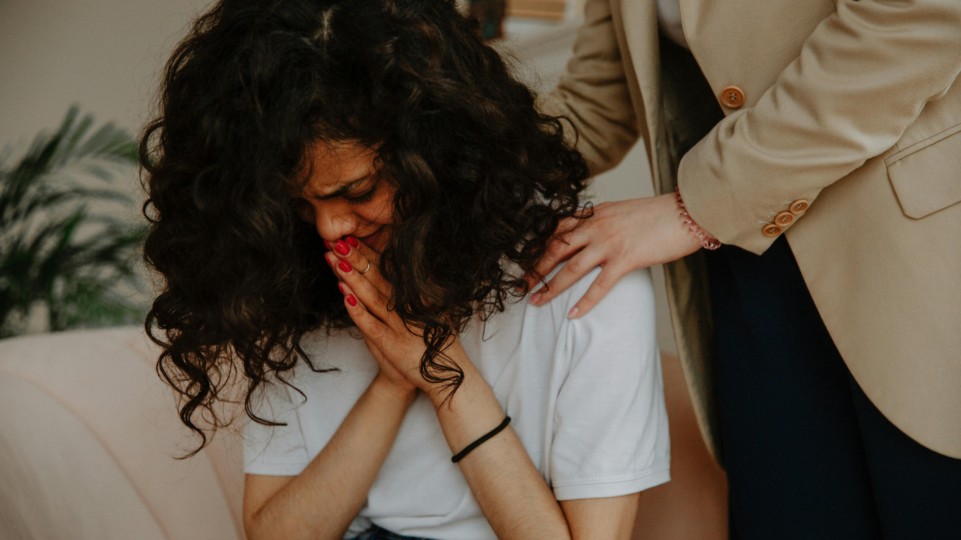 Woman crying, being consoled. A person's hand is on her shoulder. Indoor setting.