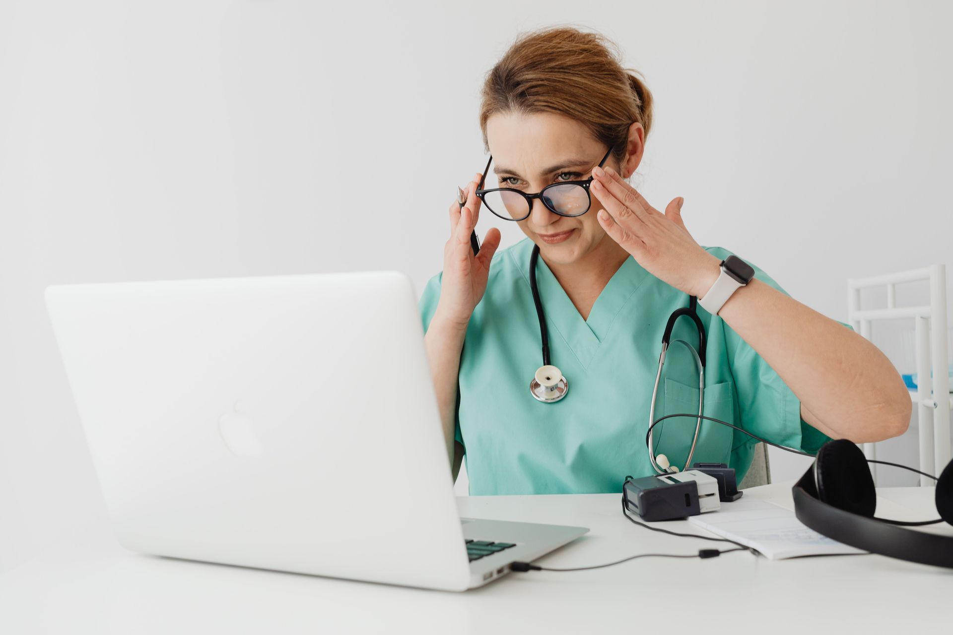 Overwhelmed healthcare leader in scrubs rubbing her eyes while working at a laptop