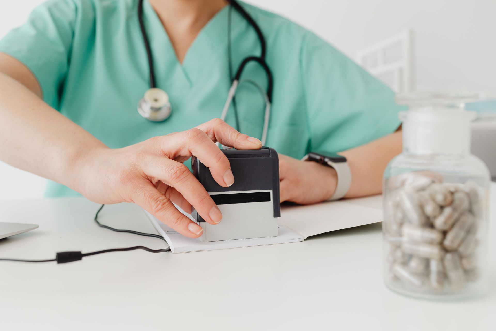 Healthcare worker stamping a prescription beside a bottle of pills on a desk