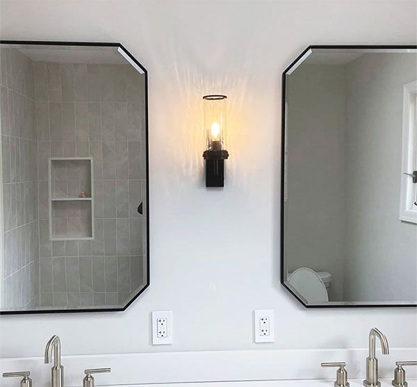 Modern bathroom vanity with two octagonal mirrors, sconces, and twin faucets under white walls.