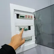 A hand pointing at circuit breakers inside an open electrical panel.