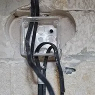 Black cables emerging from a small transparent electrical box set into a rough stone wall.