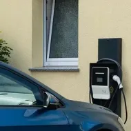Blue car parked beside a wall-mounted EV charger near a house window