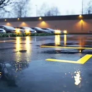 Rainy parking lot with blurred cars and yellow lane markings reflecting on wet pavement