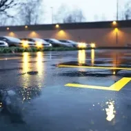 Rainy parking lot with blurred cars and yellow lane markings reflecting on wet pavement