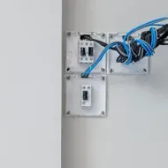 Wall-mounted electrical boxes with blue network cables and switches on a white wall