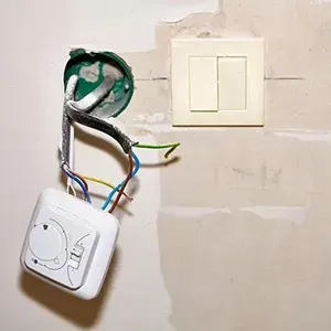 Exposed electrical wires and wall switch on a beige wall, with a loose control module hanging below.