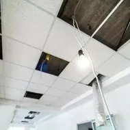 Damaged ceiling tiles with exposed wires and a hanging light in an unfinished room