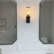 Two black-framed wall mirrors above a white vanity with a lit sconce in between.