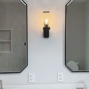 Two black-framed wall mirrors above a white vanity with a lit sconce in between.