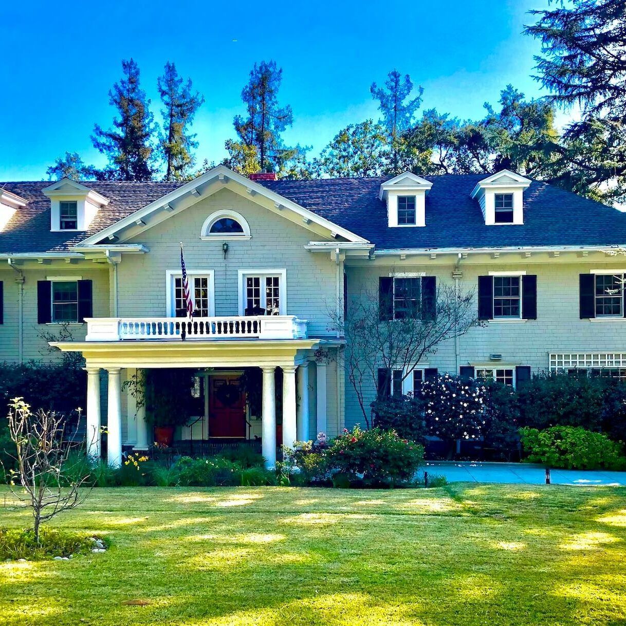 Large two-story house with a white exterior, columns, and a grassy lawn under a clear blue sky.