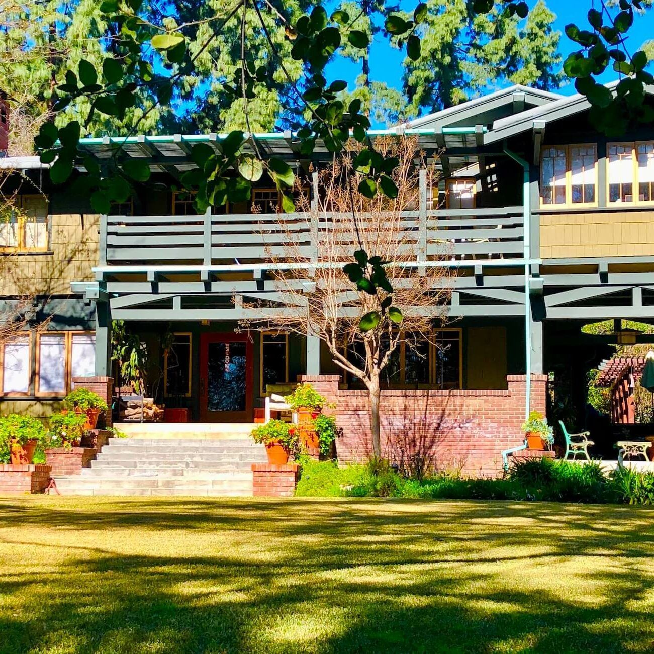 Two-story craftsman home with green trim, balcony, brick base, and large lawn.