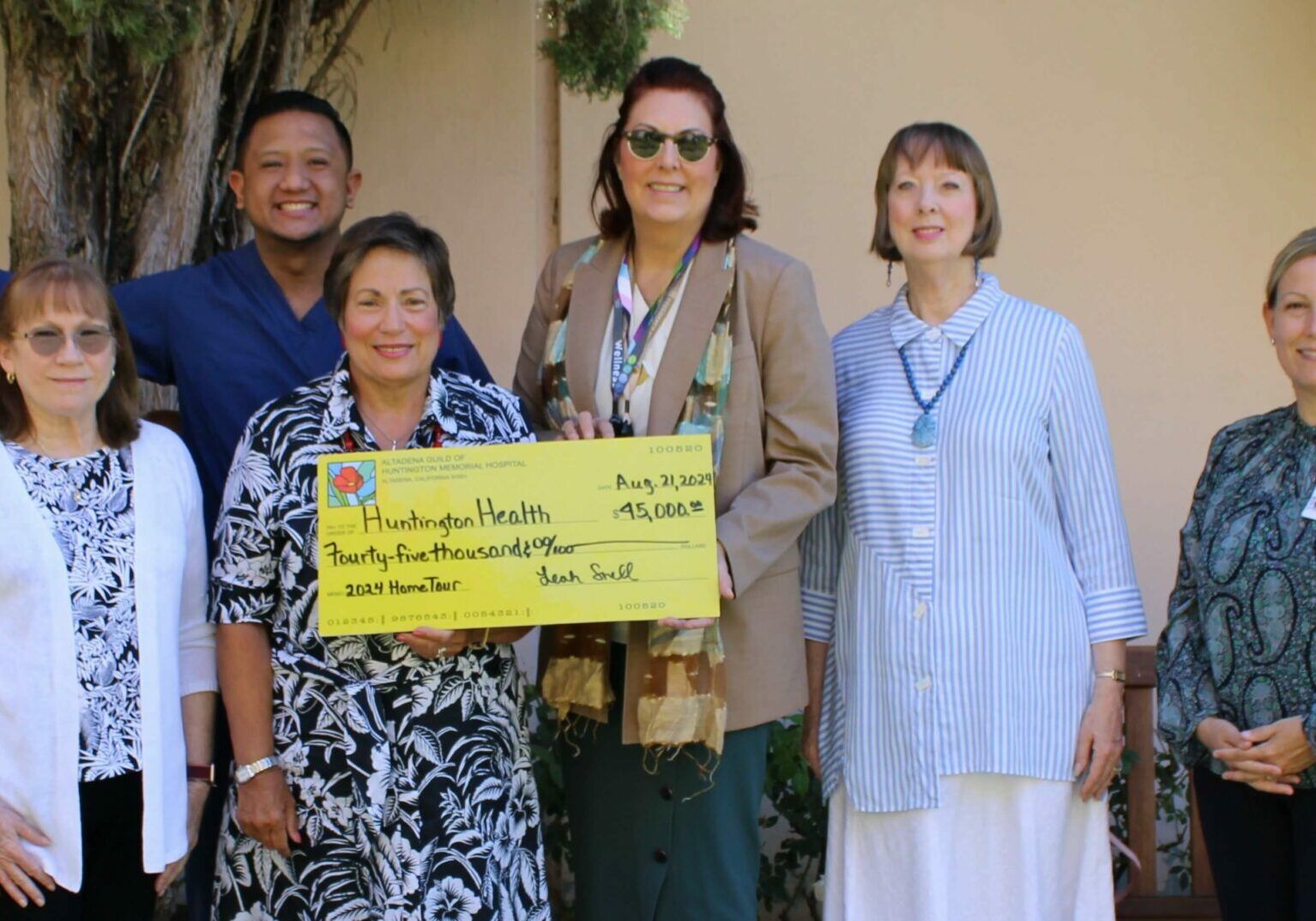 Group of people holding a large check for Huntington Health, outdoors, sunny, smiling.