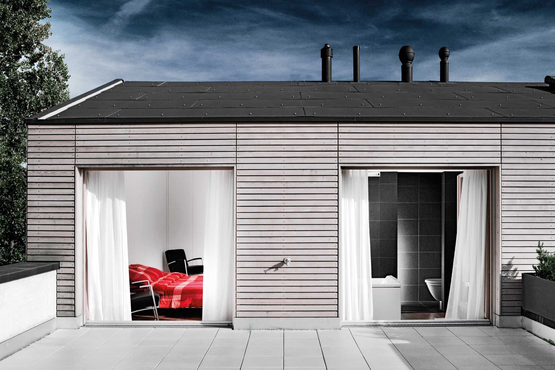 Holzgebäude mit offenen Glasschiebetüren, die ein Schlafzimmer und ein Badezimmer freigeben.