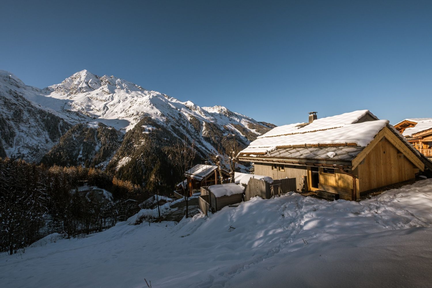 Schneebedeckte Hütte in einer Berglandschaft, Schnee auf dem Dach. Strahlend blauer Himmel.