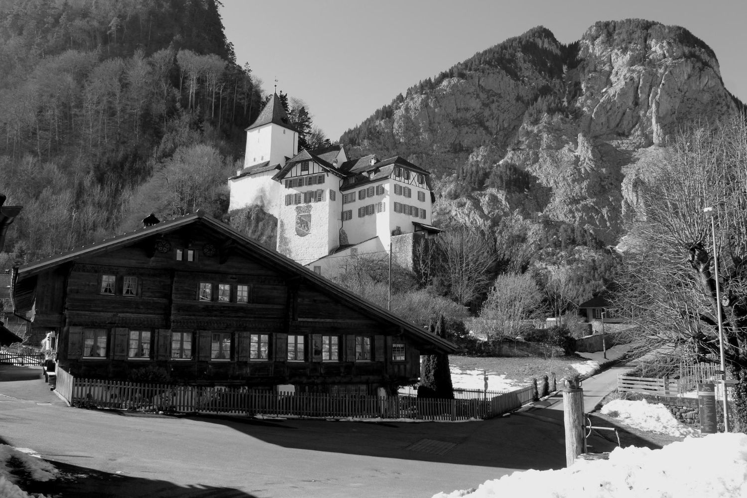 Schwarz-Weiß-Aufnahme einer Stadt an einem See mit schneebedeckten Bergen im Hintergrund.