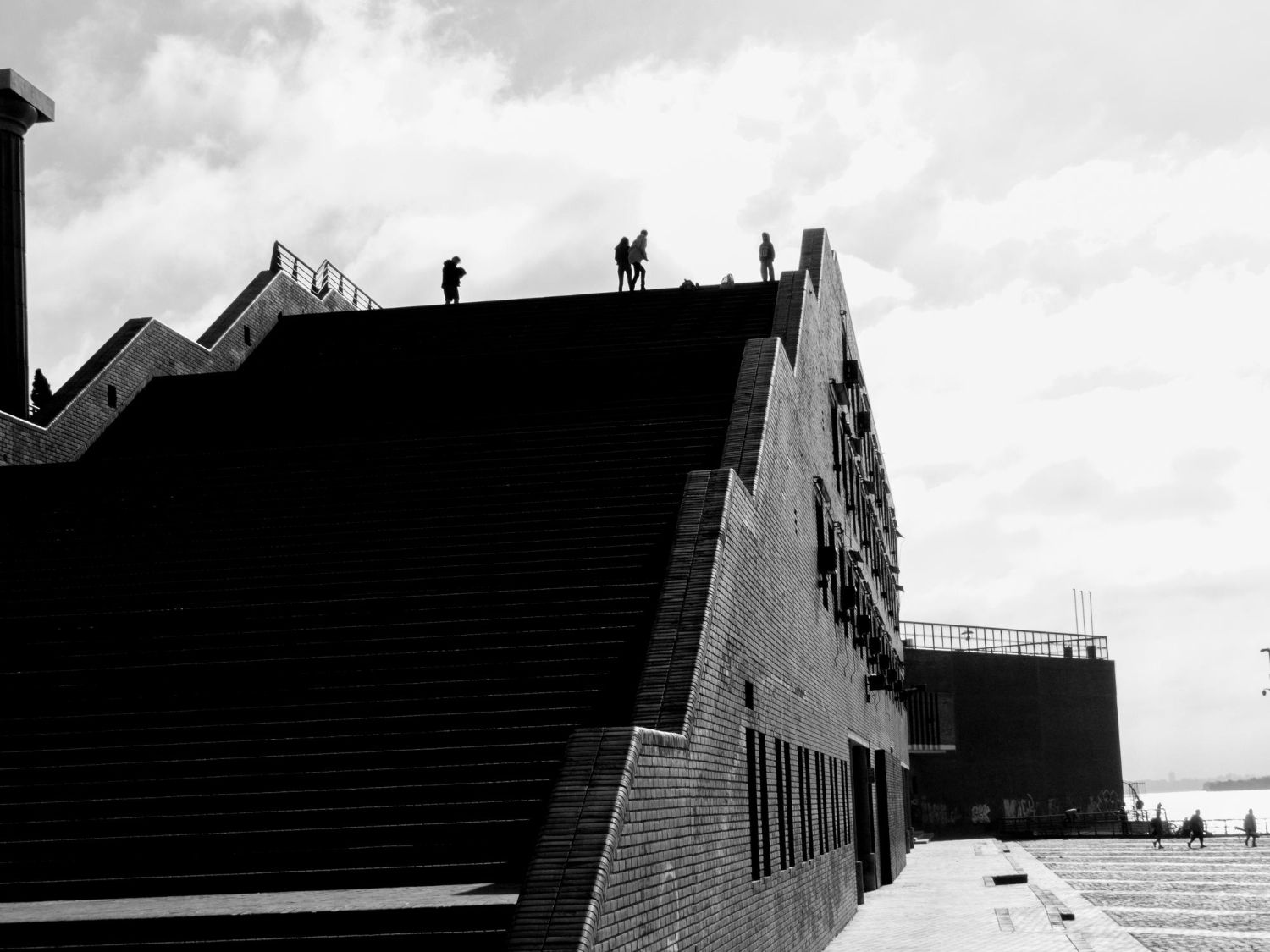 Schwarz-Weiß-Foto einer großen Backsteintreppe an einem Gebäude, auf deren Spitze Menschen stehen.