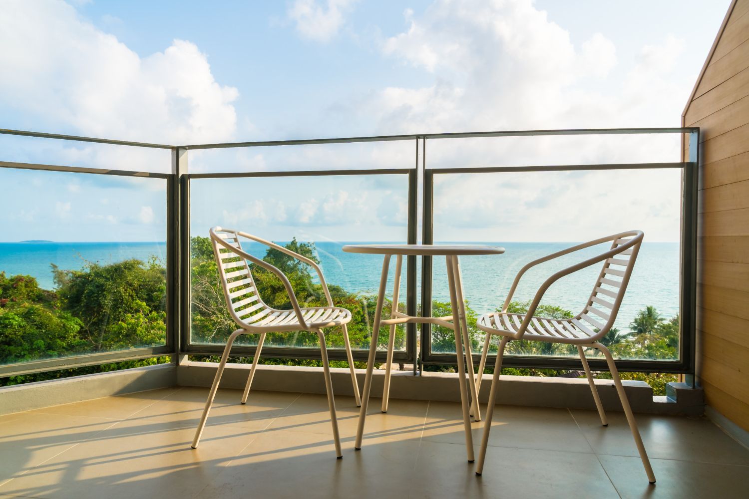 Balkon mit Metallgeländer, Pflanzen und Blick auf grüne Bäume und blauen Himmel.