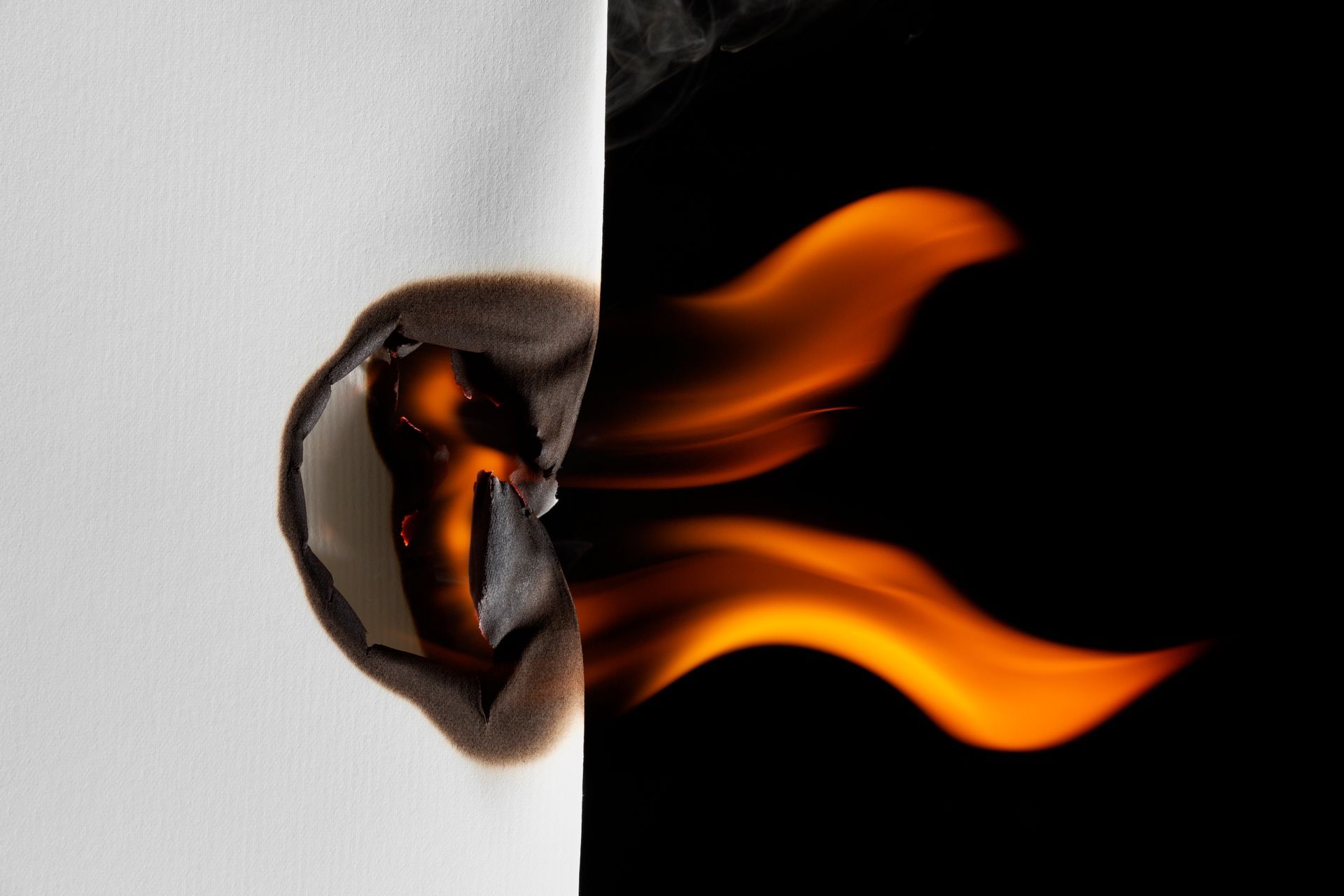 Brennendes weißes Papier mit Flammen vor schwarzem Hintergrund.