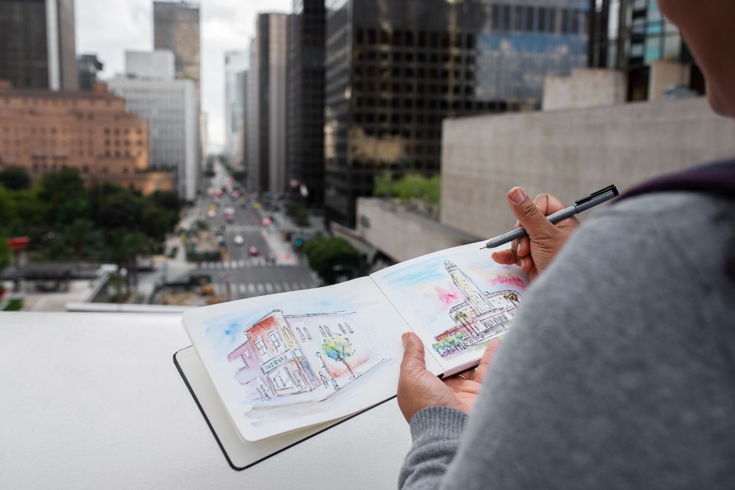 Eine Person zeichnet in ein Notizbuch ein Bild einer Stadt.