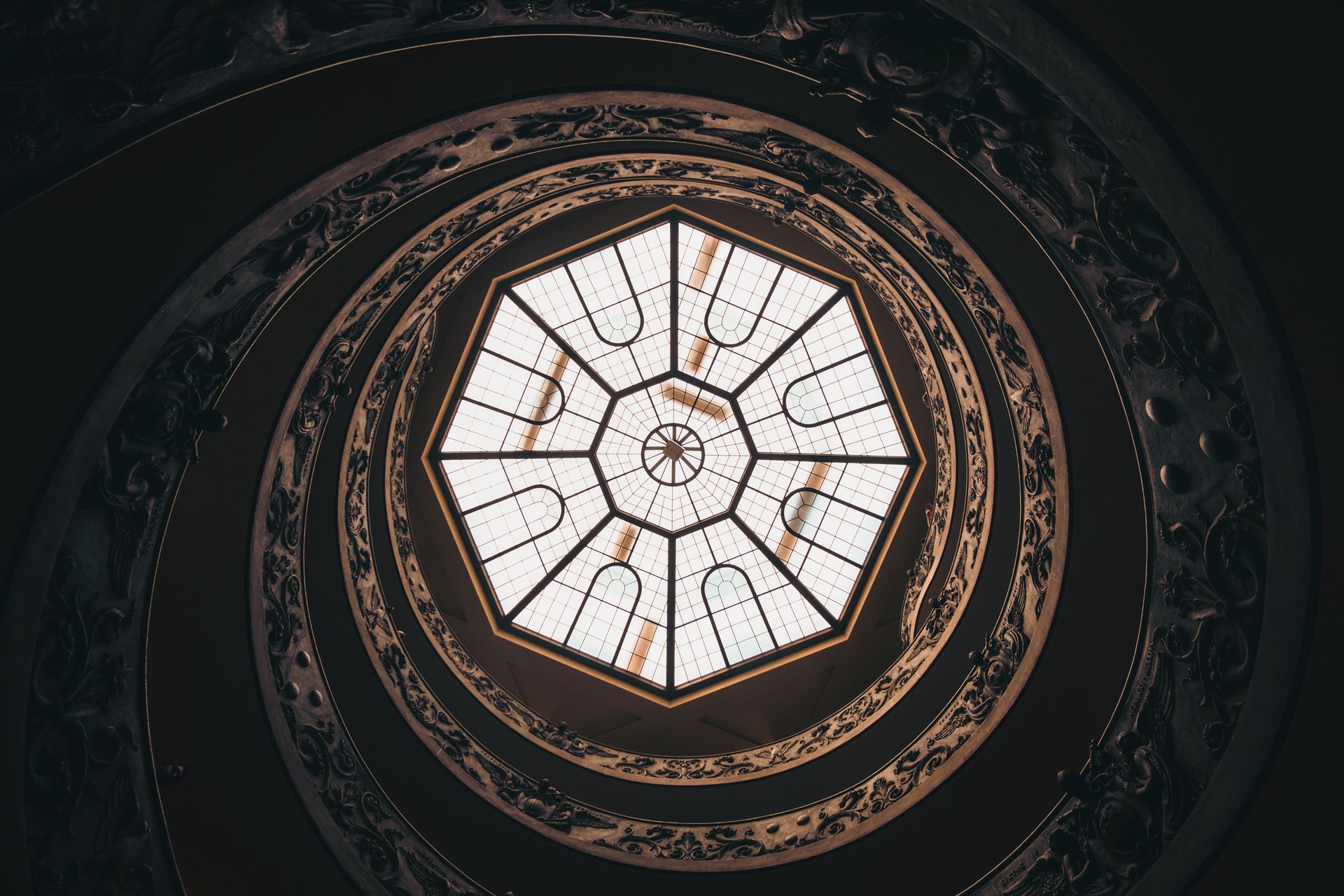 Blick nach oben auf eine Wendeltreppe mit einem runden Fenster in der Mitte.