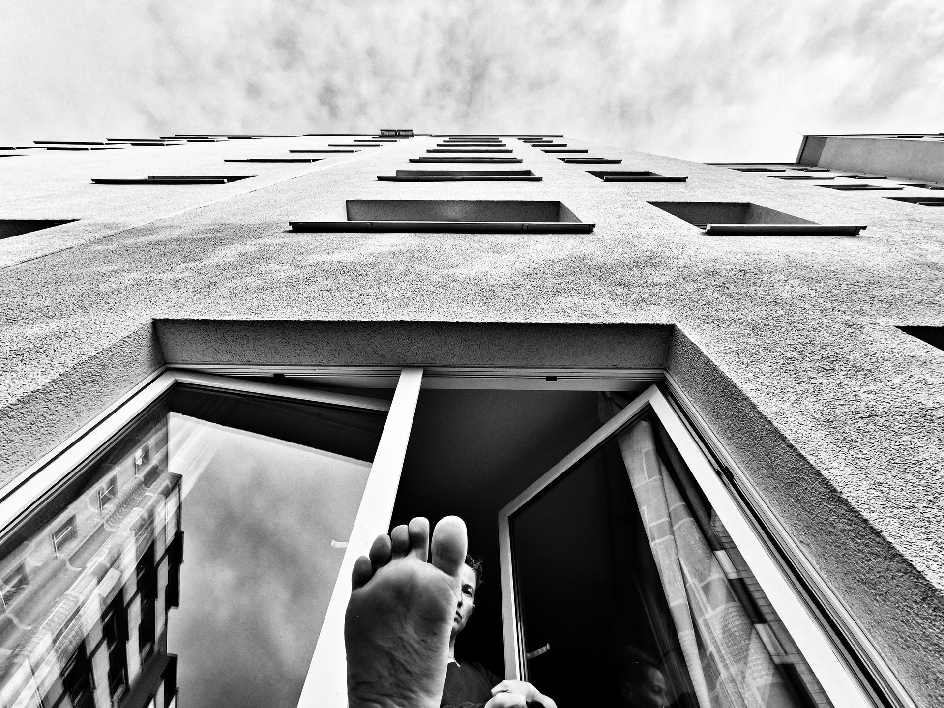 Ein Schwarzweißfoto des Fußes einer Person, der aus einem Fenster ragt.