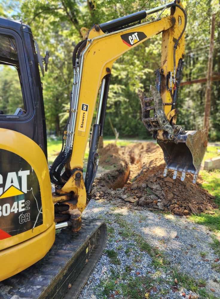 Yellow Caterpillar excavator digging earth near trees in a sunny setting.