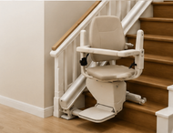 Woman seated on a stair lift beside a carpeted staircase in a home interior
