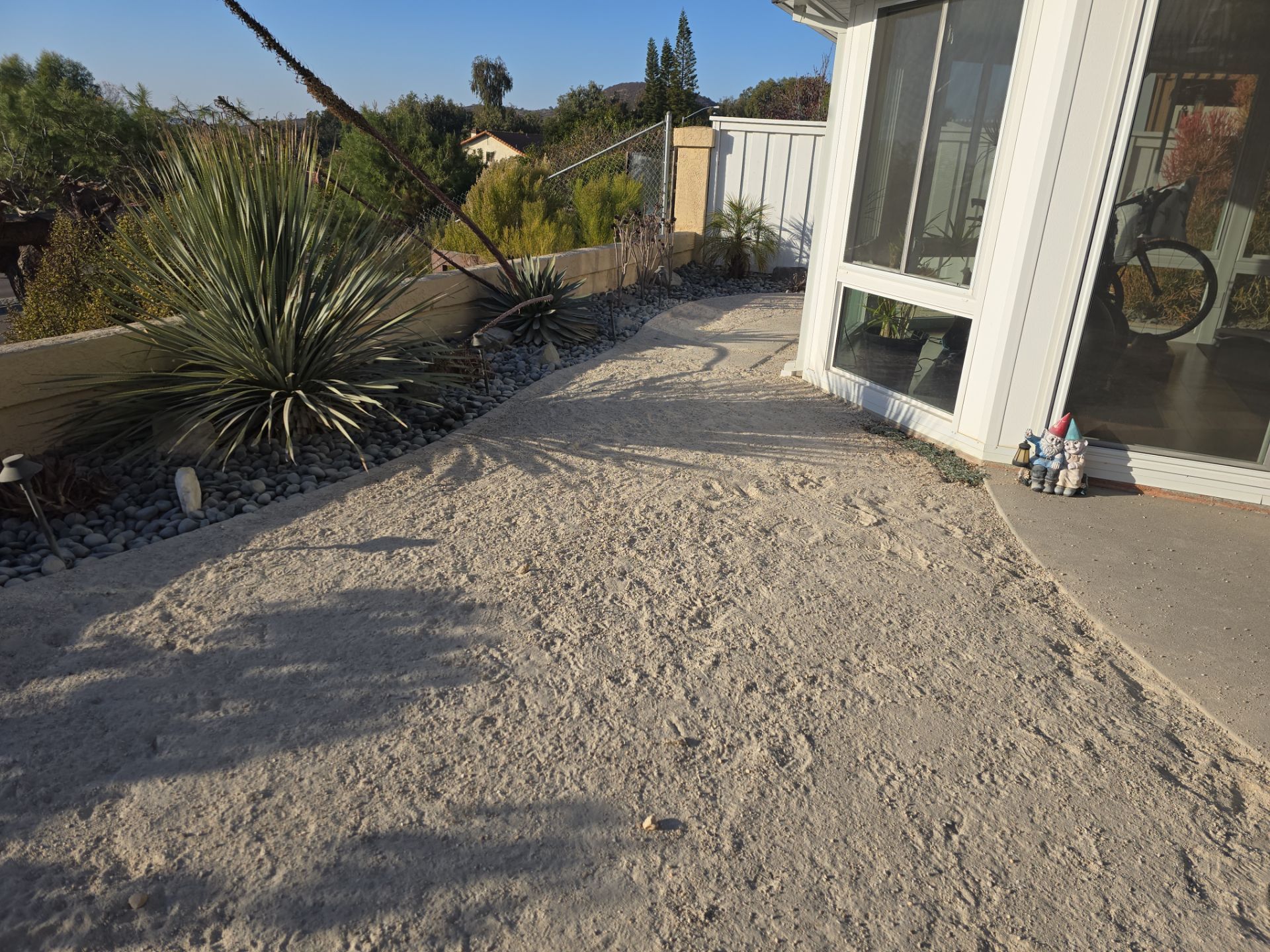 A gravel-covered pathway next to a white house with a screened porch and drought-tolerant landscaping.