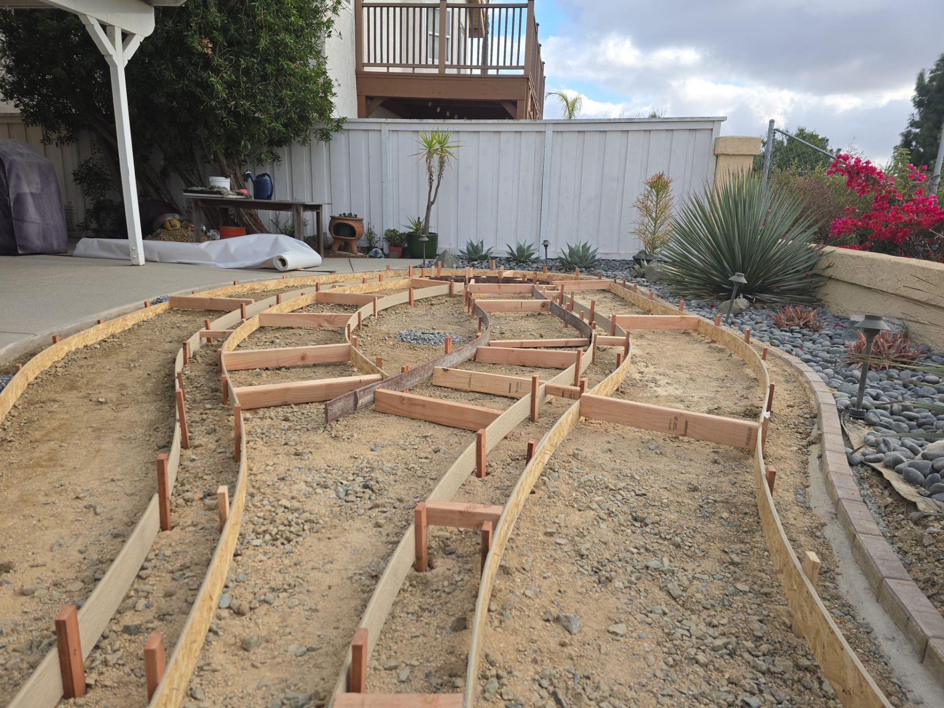 Garden bed project: wooden forms outline winding pathways filled with gravel and sand, backyard setting.