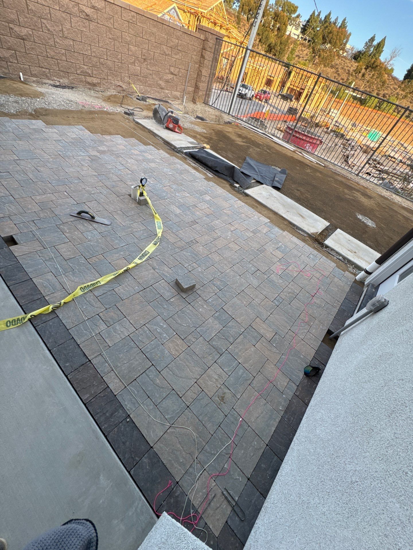 Brick patio with black border, construction zone behind a fence. Yellow caution tape.